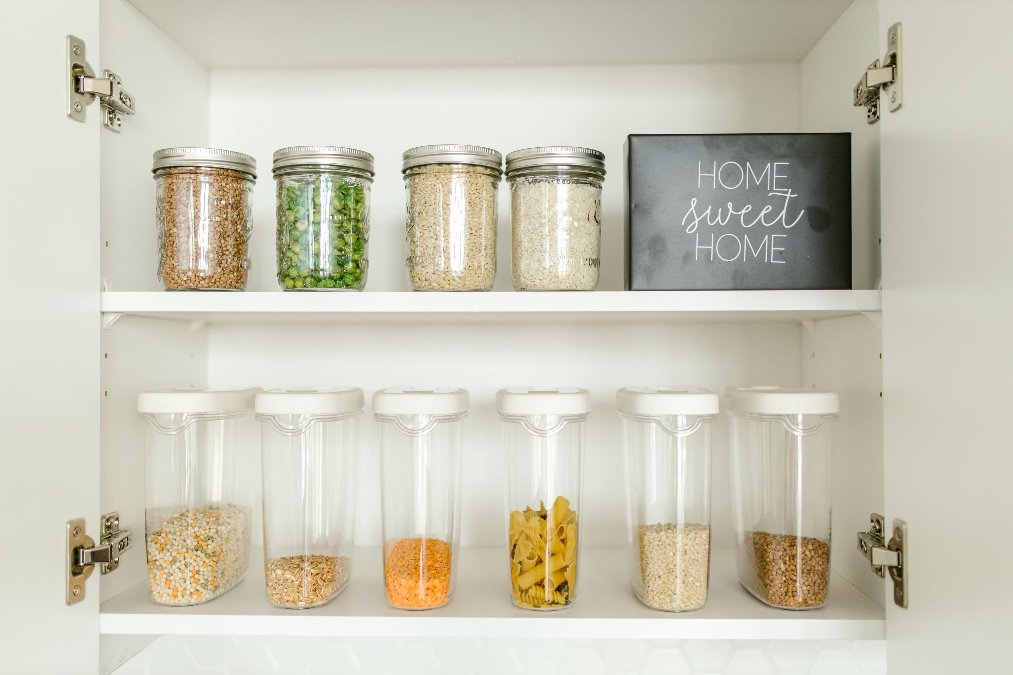 Organized white cabinet shelves with glass jars, plastic containers, and a Home Sweet Home sign.