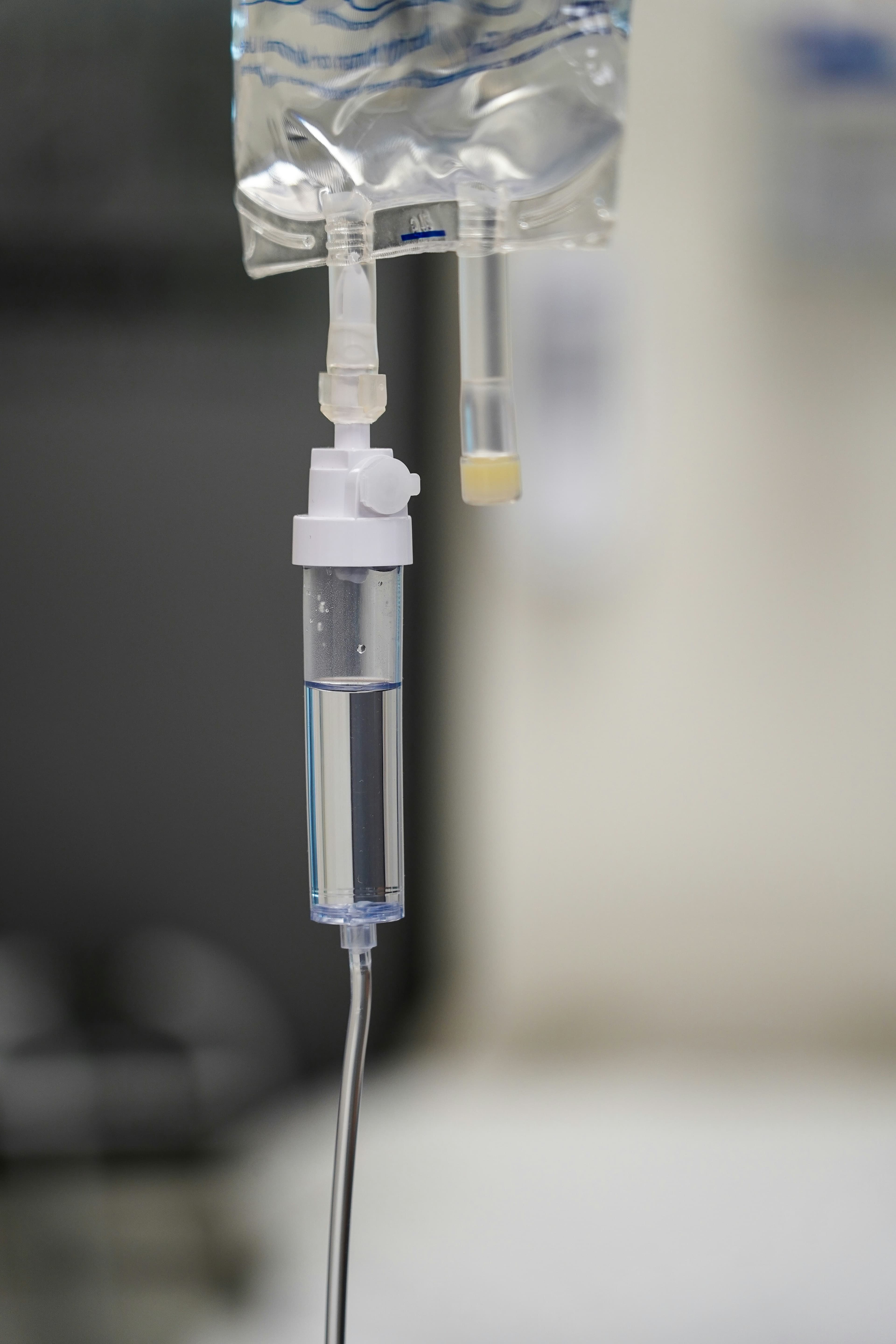 Close-up of an intravenous drip bag and chamber with clear liquid in a medical setting.